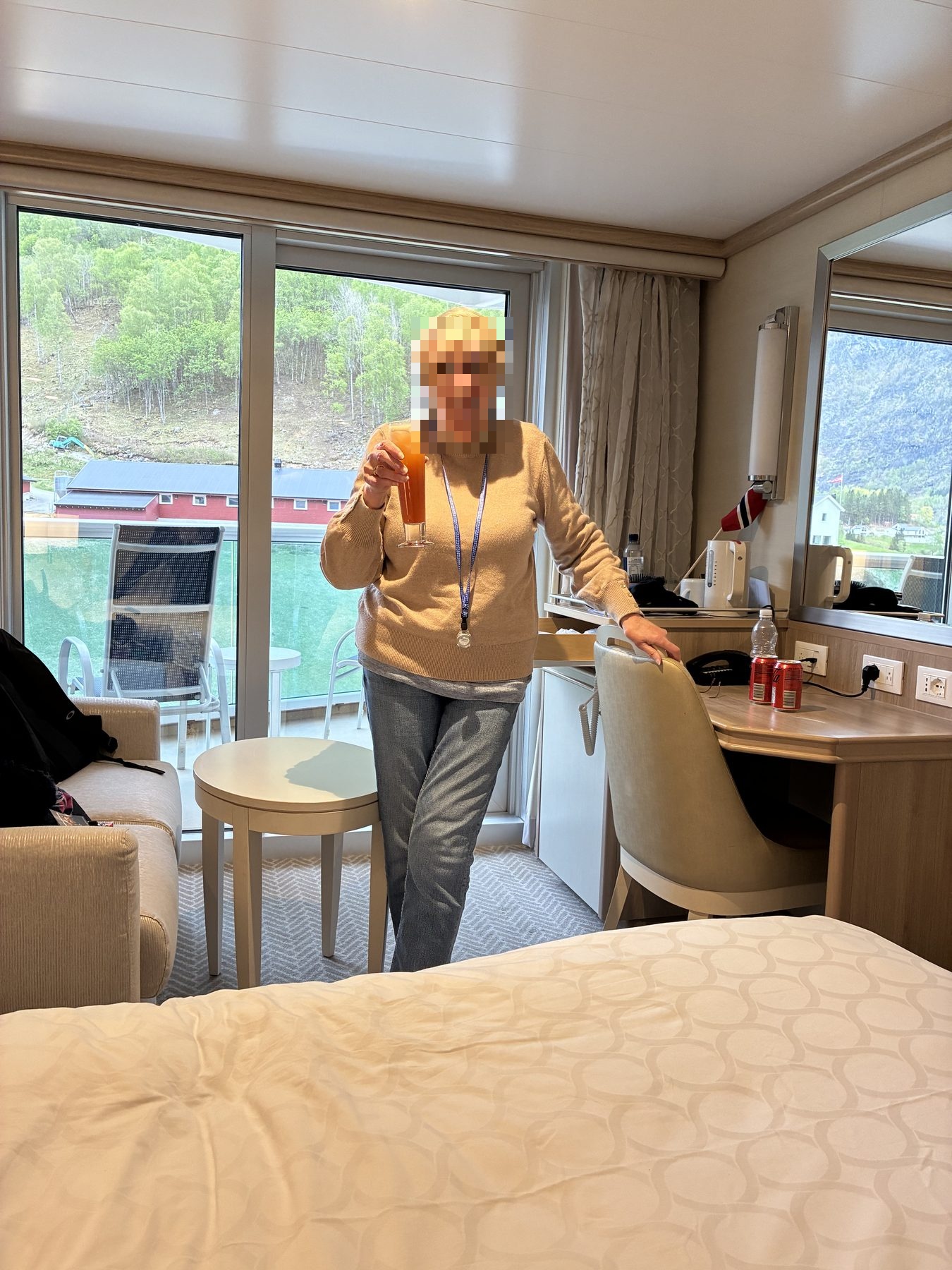 Mum holding an orange cocktail in the cabin, fjord visible through the balcony doors